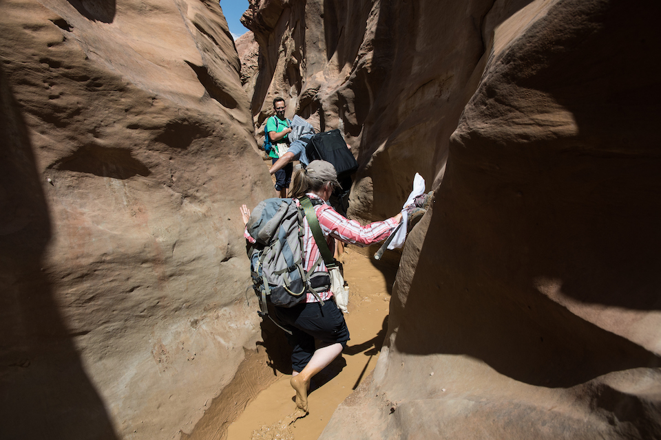 Image of people walking thru mud puddle in slot canyon.
